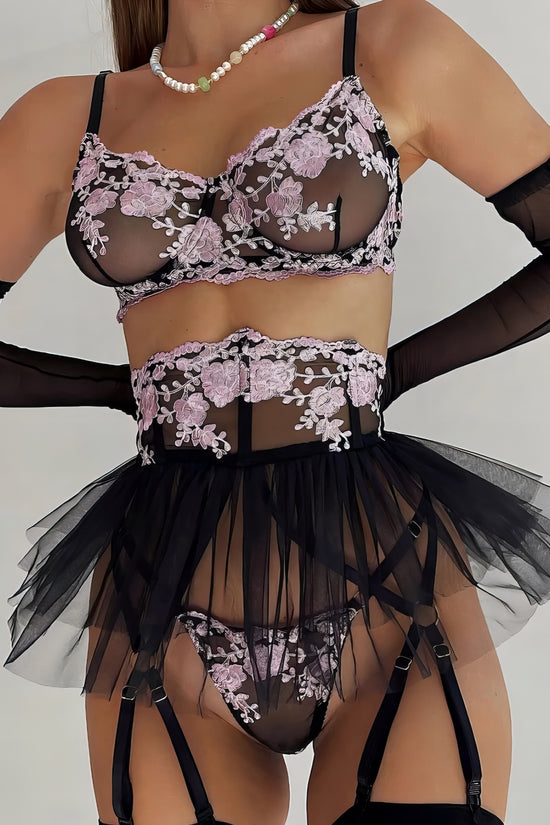 Woman wearing a black mesh 2-piece lingerie set with purple embroidery, posing on a white background