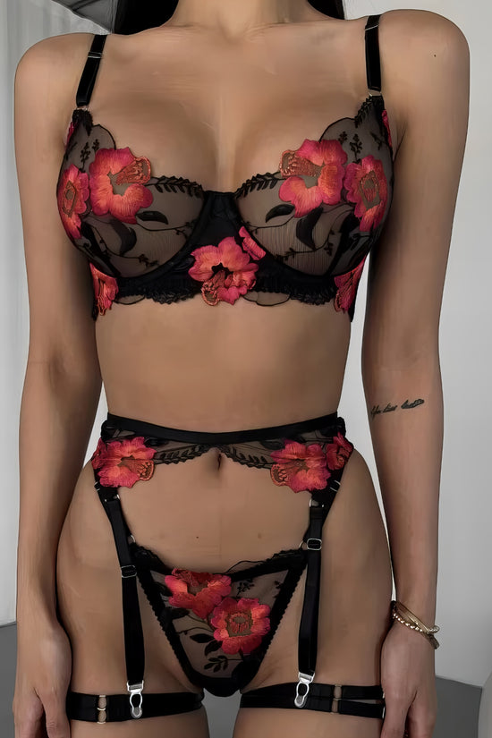 Woman wearing a luxury black mesh 3-piece lingerie set with pink floral embroidery, including underwire bra, garter belt, and matching thong
