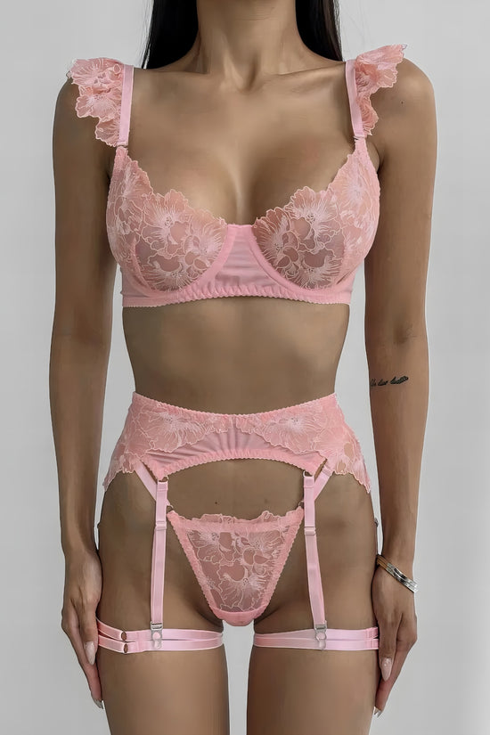 Woman wearing a luxury pink mesh 3-piece lingerie set with embroidery, including underwire bra, garter belt, and matching thong 