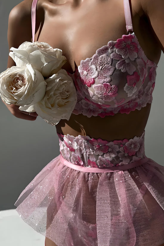 Woman wearing a luxury pink mesh 3-piece lingerie set with pink floral embroidery, including underwire bra, garter belt, and matching thong