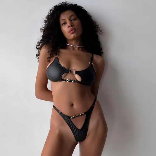 Woman wearing a black leather 2-piece lingerie set , posing on a white background