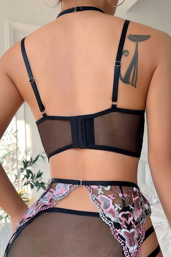 Woman wearing a black mesh 2-piece lingerie set with pink embroidery, posing on a white background