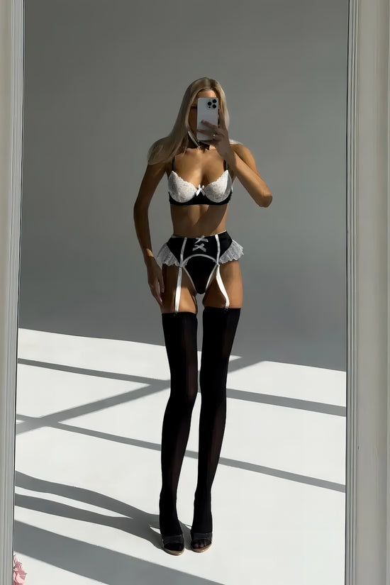 Woman wearing a luxury black mesh 3-piece lingerie set with pink floral embroidery, including underwire bra, garter belt, and matching thong